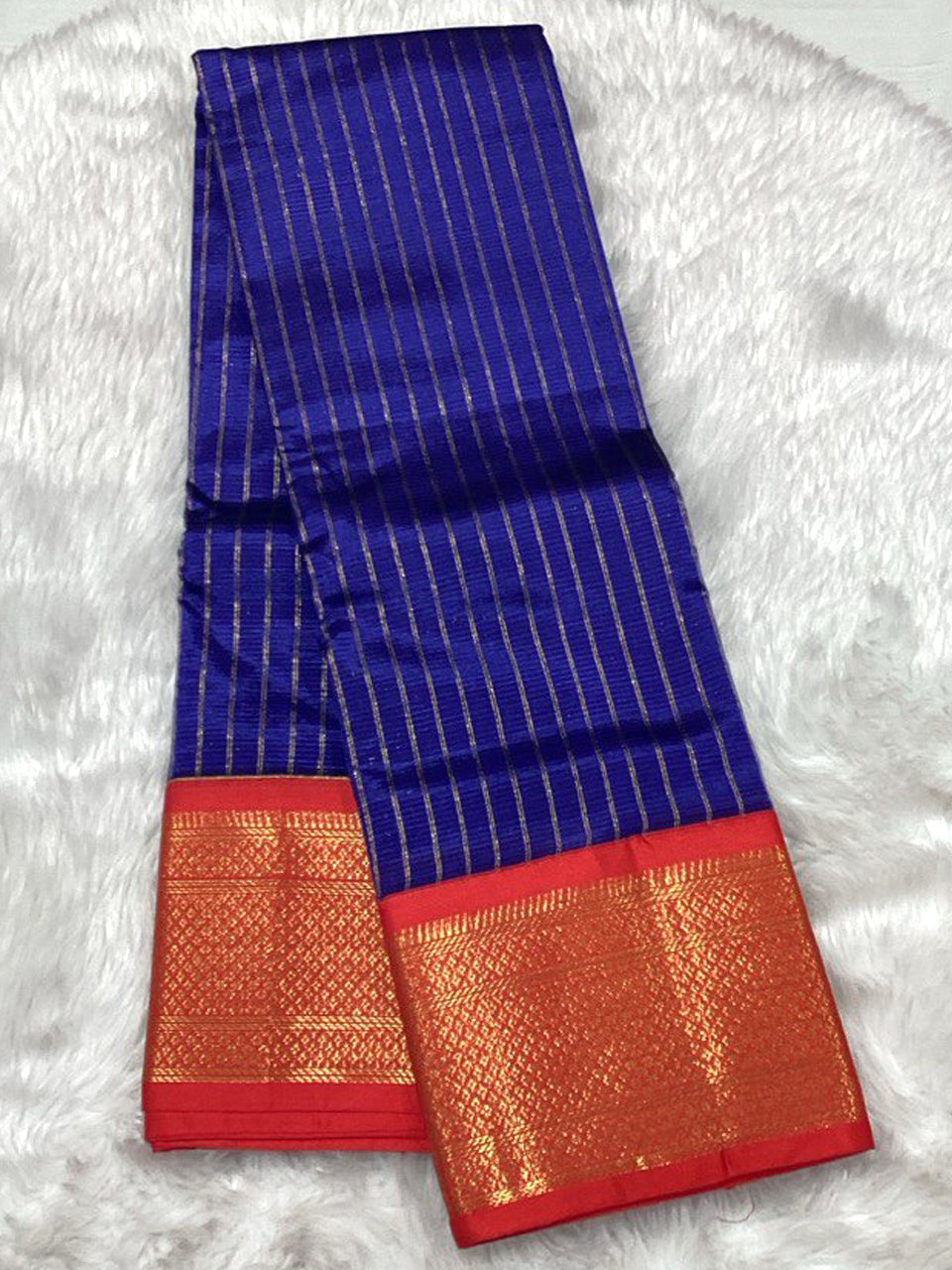 A royal blue Assam pattu saree featuring vertical gold stripes and a traditional heavy red and gold zari border.