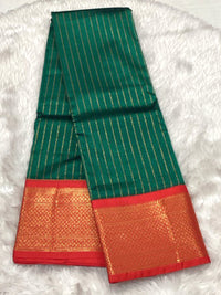 An emerald green Assam silk saree featuring shimmering gold vertical stripes and a broad red border with elaborate gold zari weaving.