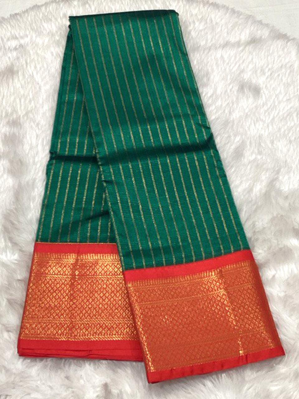An emerald green Assam silk saree featuring shimmering gold vertical stripes and a broad red border with elaborate gold zari weaving.