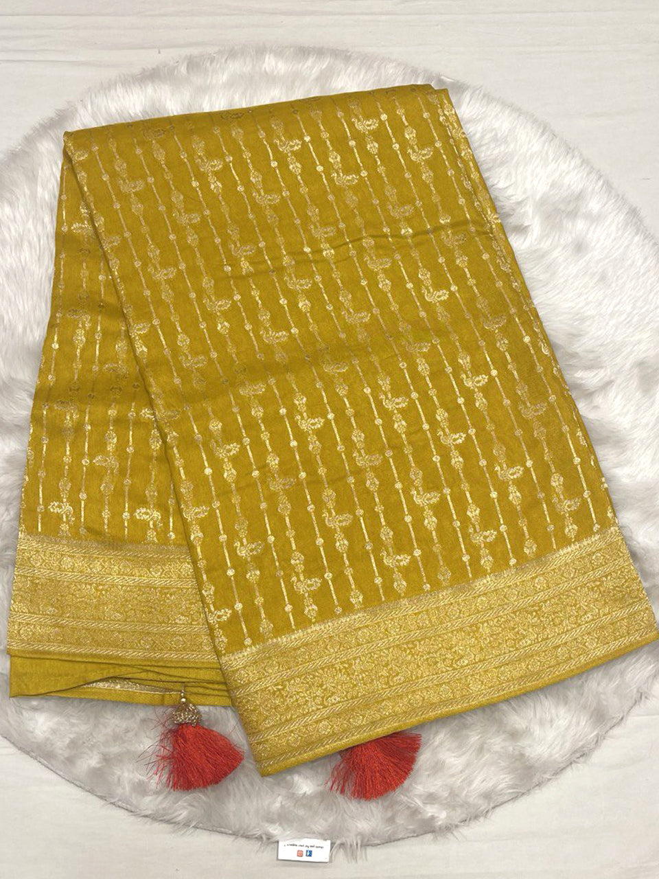 Mustard yellow Banarasi soft silk saree with vertical gold zari lines and bird motifs, finished with red tassels.