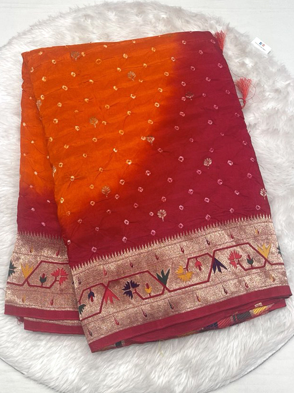 A vibrant orange and maroon shaded Bandhani saree featuring hand-tied dots and a rich Banarasi silk border with traditional temple zari work.
