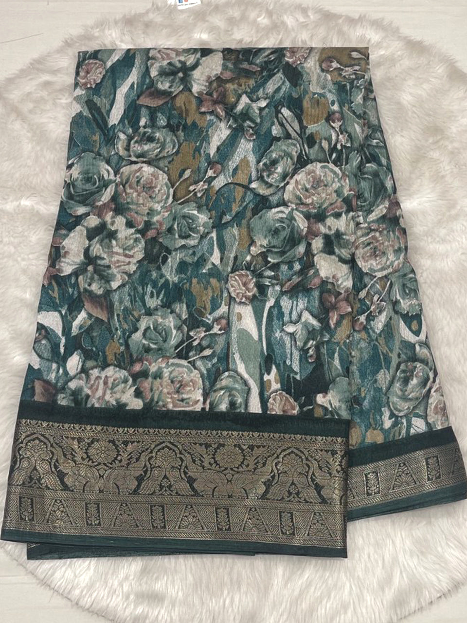 Teal blue crushed fancy saree with large white floral prints and a broad dark green zari woven border.