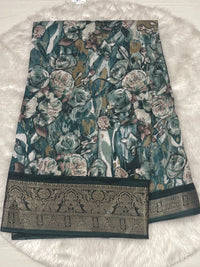 Teal blue crushed fancy saree with large white floral prints and a broad dark green zari woven border.