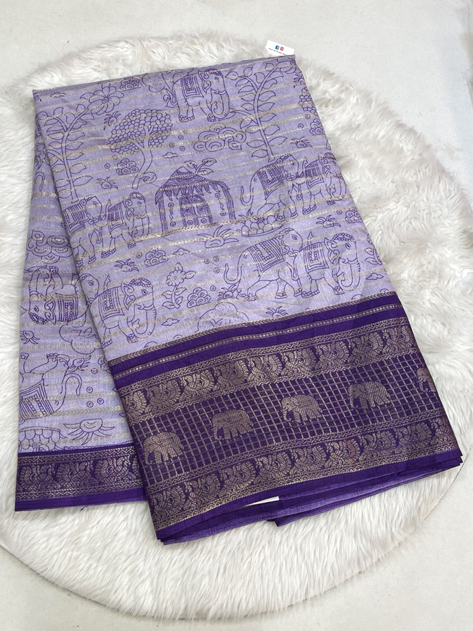 Lavender Dola silk saree with all-over horizontal zari weaving, traditional village scenery prints, and a deep purple contrast border with elephant and peacock motifs.