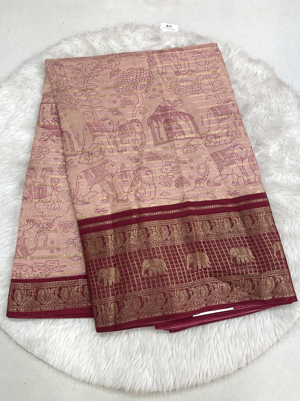 Peach-toned Dola silk saree featuring gold zari lines, intricate elephant and hut prints, and a rich maroon contrast zari weaving border.