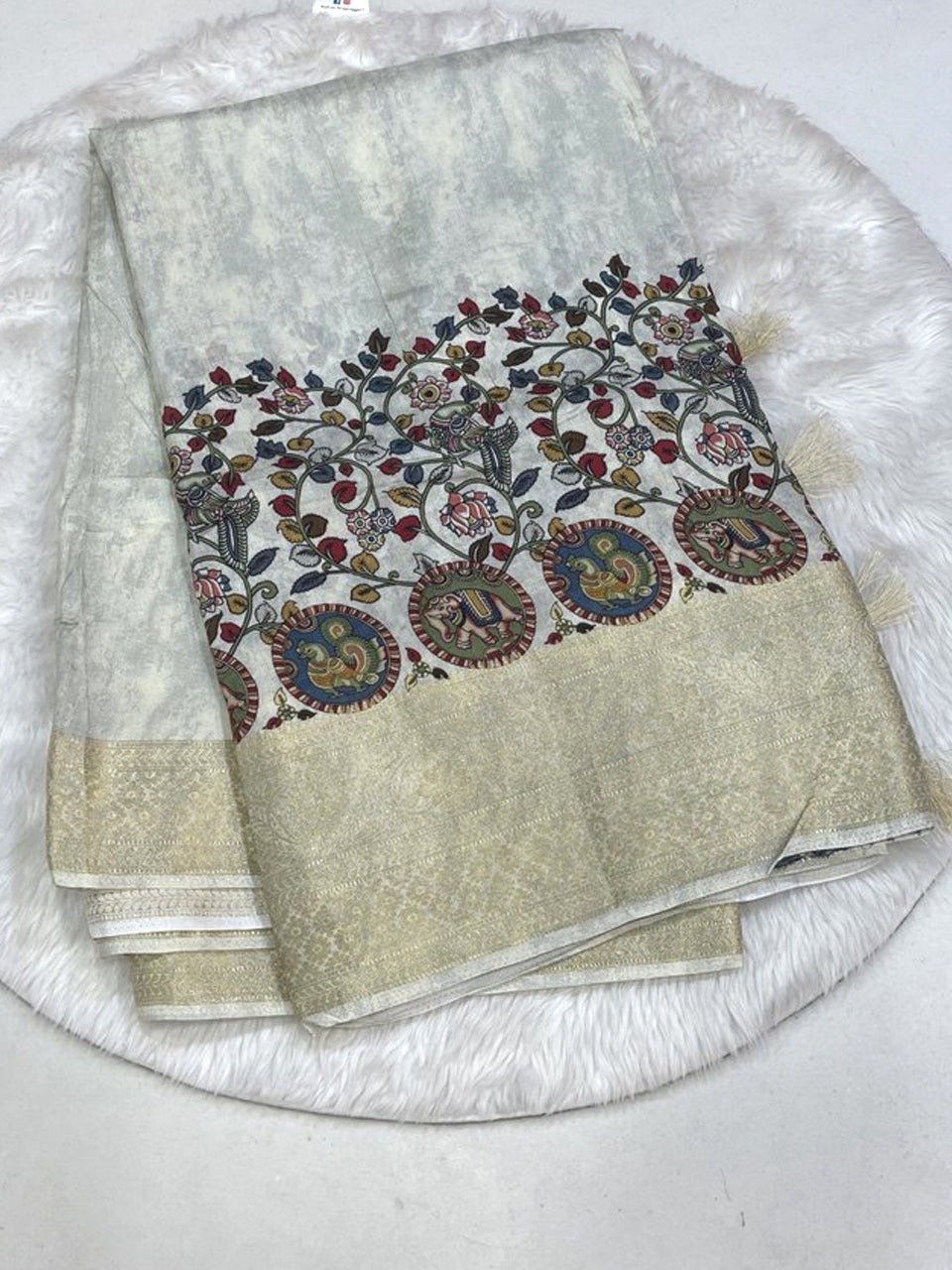 Off-white Mashru silk saree featuring hand-painted Pen Kalamkari border with multi-color floral, peacock, and elephant motifs and a golden zari tissue edge.