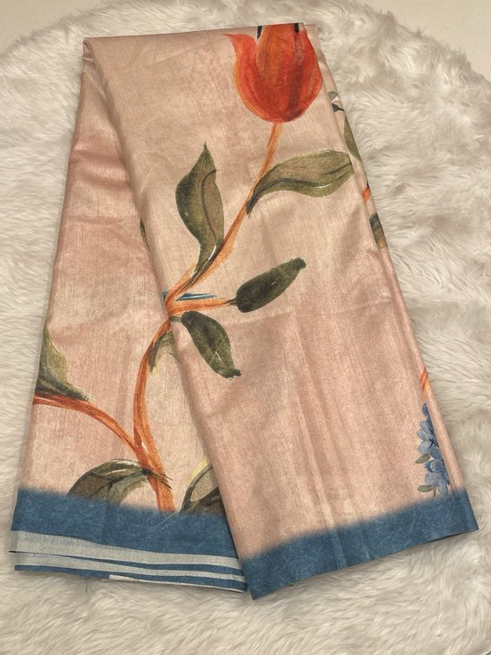 A champagne-beige raw silk saree featuring a large-scale hand-painted style floral print with a vibrant orange tulip and green leaves, finished with a contrasting slate blue border and silver zari stripes.