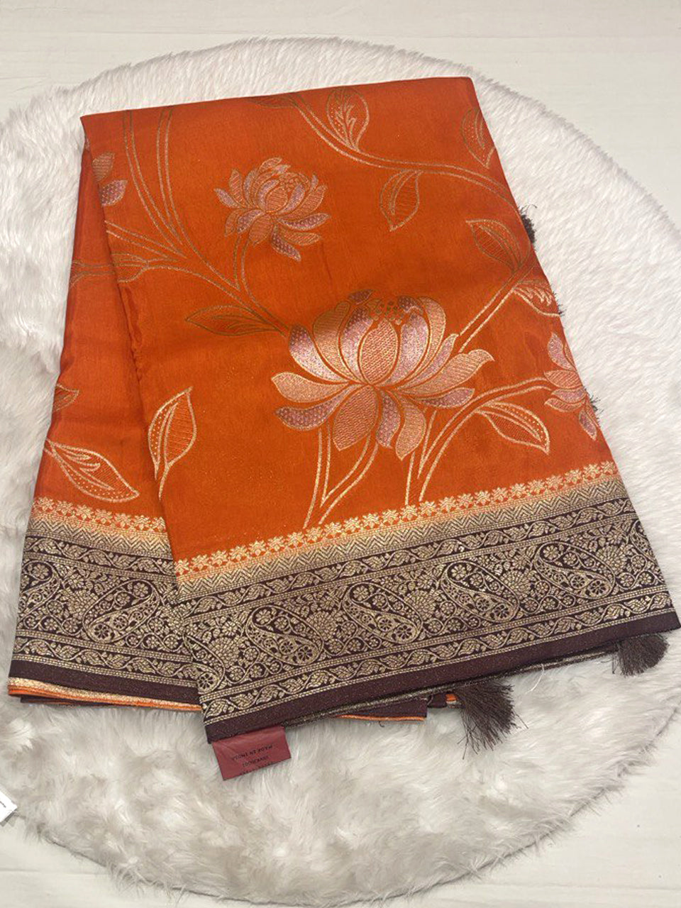 Vibrant orange Russian viscose saree with dark brown designer border and silver floral weave.