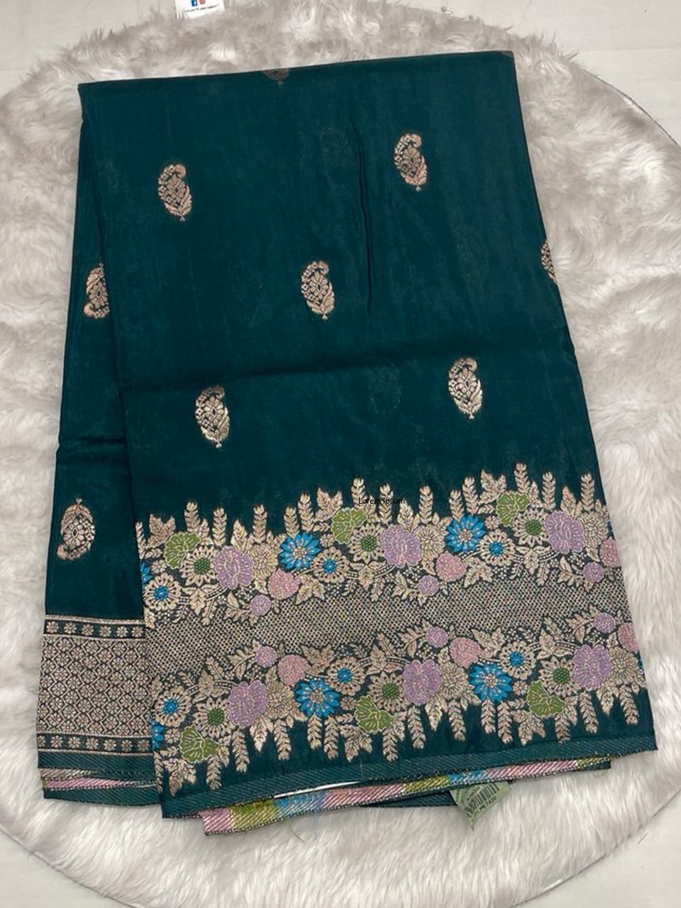 Deep teal Samurai Satin saree featuring gold paisley butties and a thick floral zari border with blue and purple highlights.