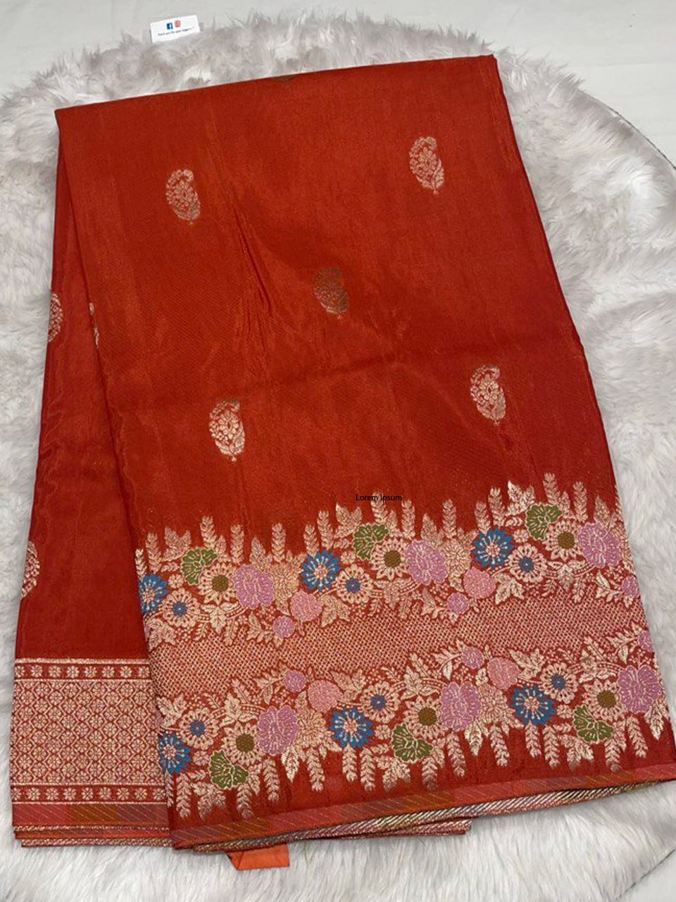 Rich rustic red Samurai Satin saree with intricate gold zari work and a multi-color floral meenakari border.