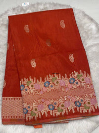 Rich rustic red Samurai Satin saree with intricate gold zari work and a multi-color floral meenakari border.