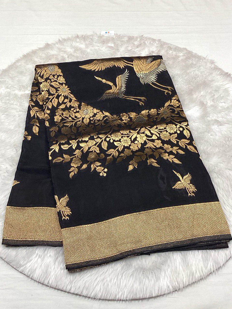 Elegant jet black Mashru Satin saree decorated with intricate gold Zari embroidery of birds in flight and floral vines, finished with a textured gold border.